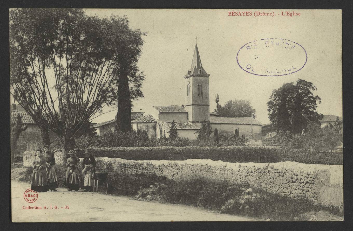 Carte postale ancienne de Bésayes, quatre femmes en tablier sur une route devant un mur de pierre, avec l'église et son clocher à flèche pointue derrière