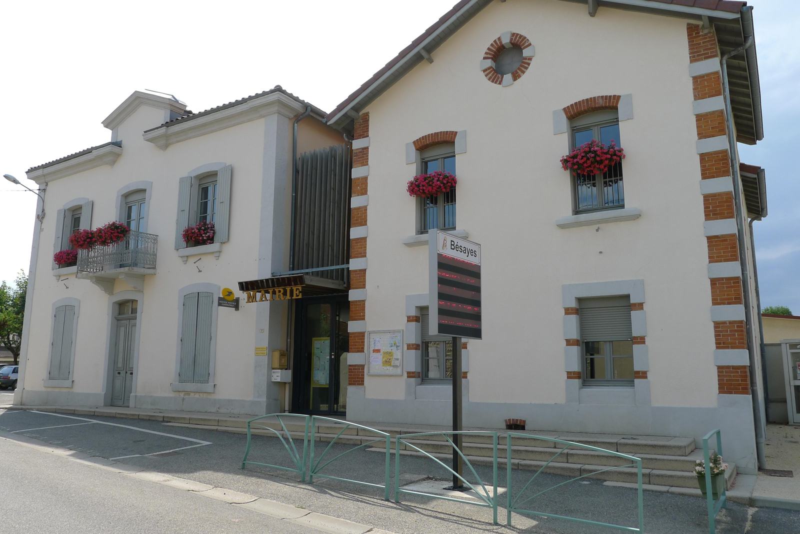 La mairie de Bésayes, deux bâtiments clairs aux encadrements de briques reliés par une entrée vitrée, avec des géraniums aux fenêtres