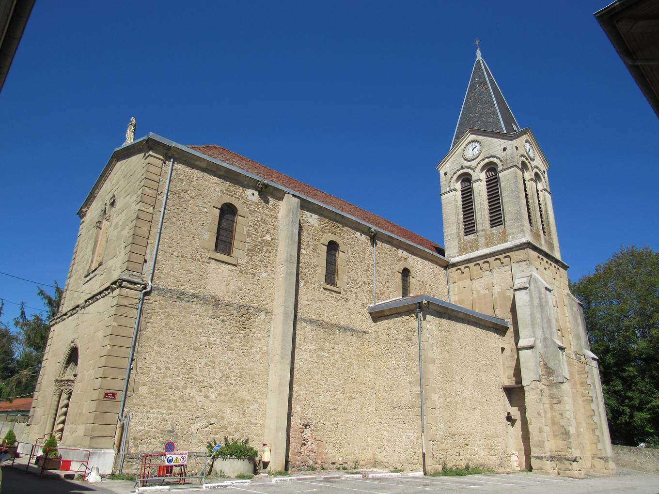 L'église Saint-Jean-Baptiste de Châtillon-Saint-Jean, nef de pierre ocre et clocher carré à horloge surmonté d'une flèche d'ardoise, sous un ciel bleu