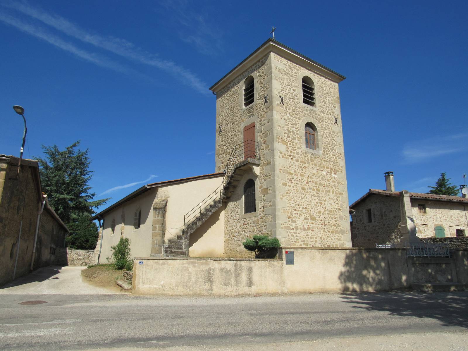 L'église de Chavannes, nef basse crépie et haut clocher carré de pierre avec un escalier extérieur, derrière un mur, et le monument aux morts à droite