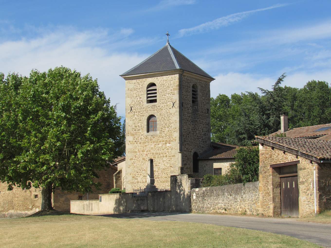Le clocher carré en pierre de l'église de Chavannes, coiffé d'un toit d'ardoise, derrière un mur et un grand platane, sous un ciel bleu