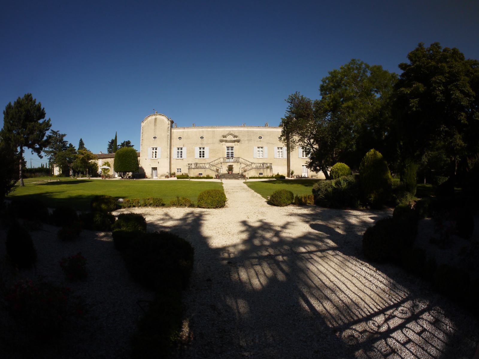 La façade est du château de Genas, longue et claire, avec un escalier double au centre et une tour arrondie à gauche, au bout d'une allée de gravier entre deux pelouses