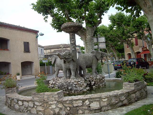La fontaine de Cléon-d'Andran, trois éléphants de pierre grise autour d'une colonne, dans un bassin rond en pierres sous des platanes