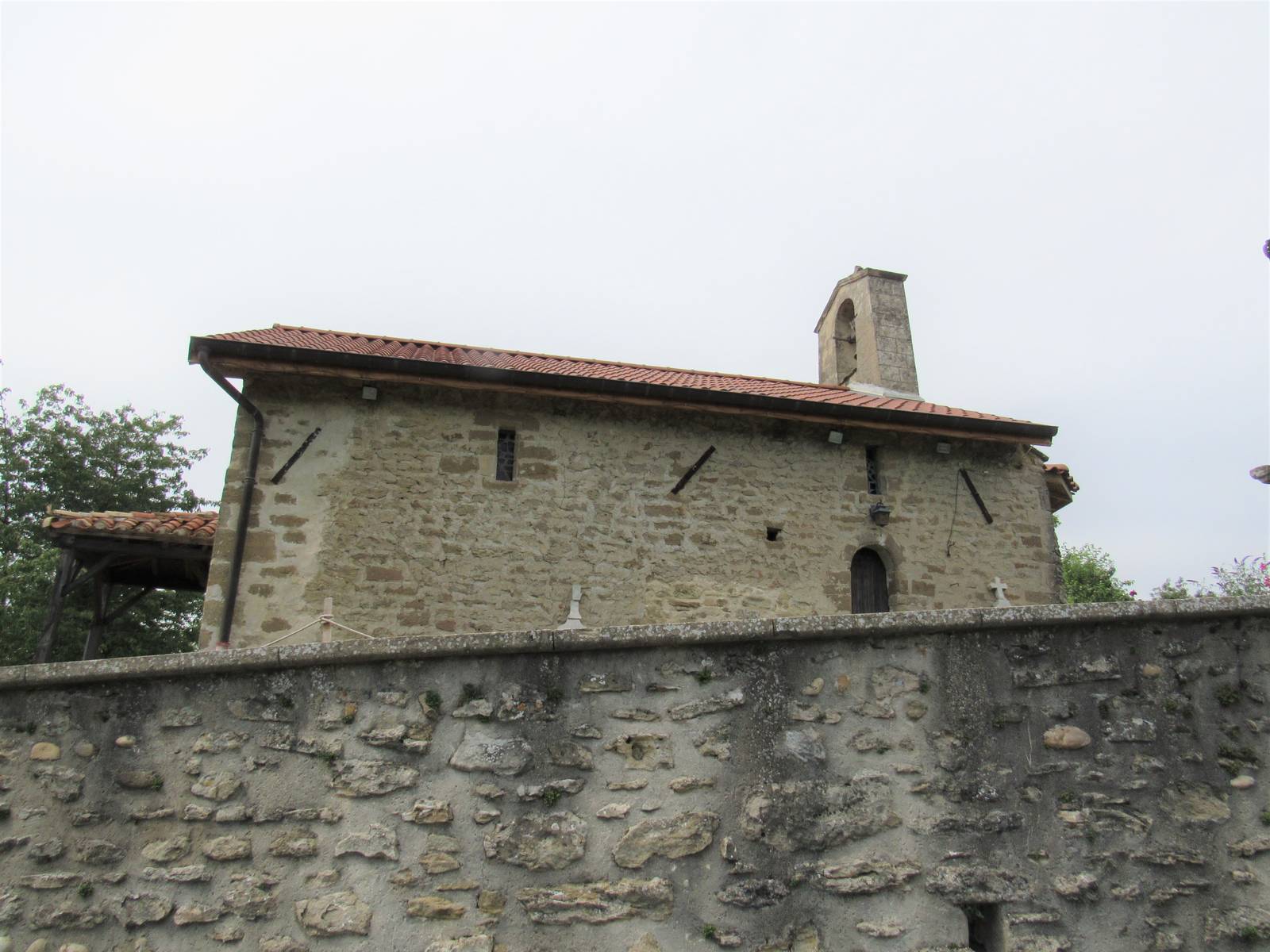La chapelle Saint-Roch de Crépol, petit édifice de pierre aux tuiles rouges avec son clocher-mur, derrière un haut mur de galets