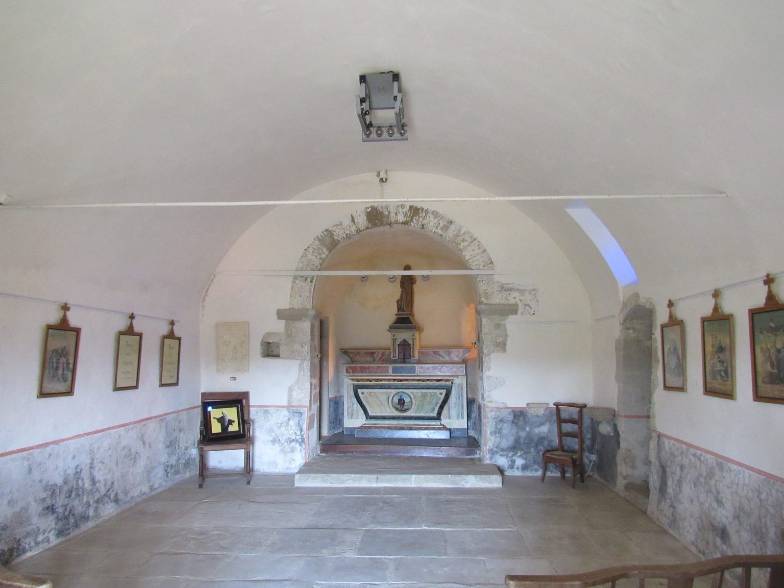 L'intérieur blanc et voûté de la chapelle Saint-Roch, l'autel sous un arc de pierre au fond, des tableaux du chemin de croix aux murs