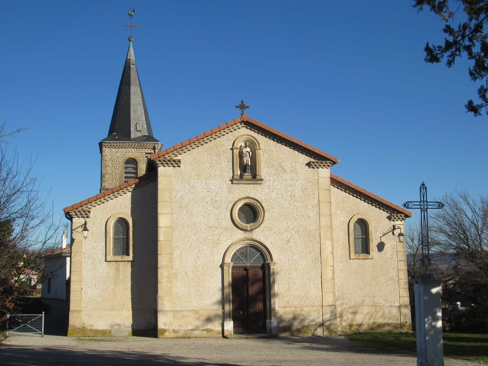 L'église Saint-François-Régis d'Épinouze, façade claire à fronton, statue en niche et clocher pointu