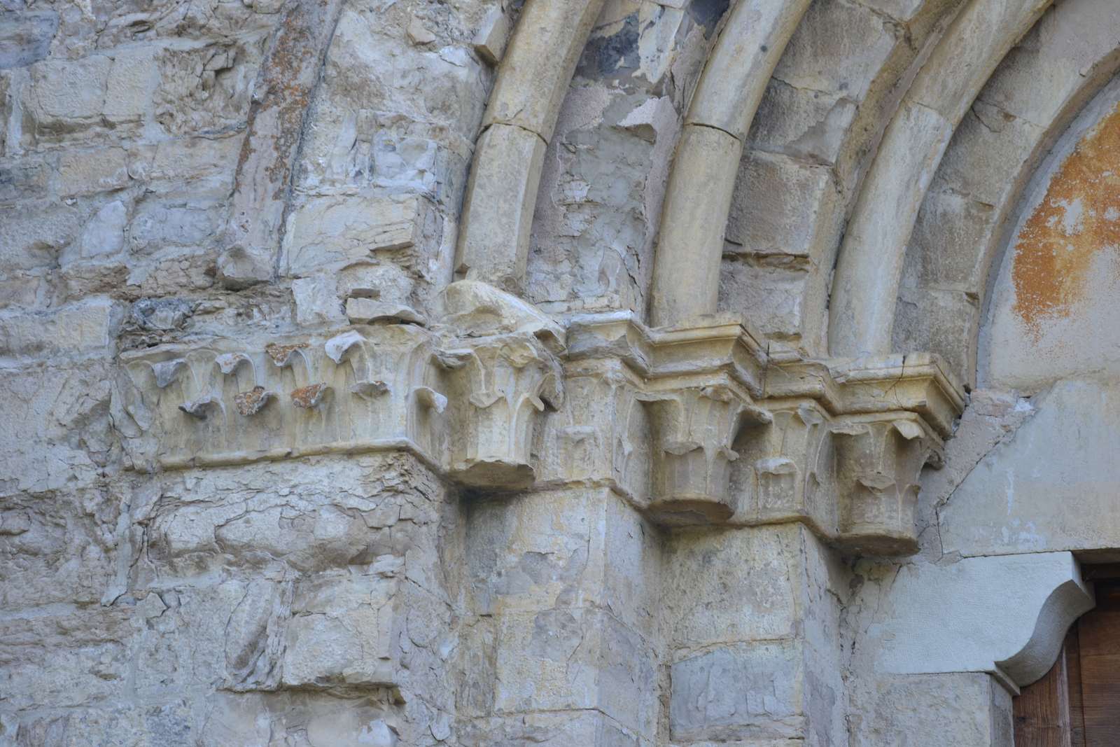 Détail du portail de Notre-Dame-de-Calma, une rangée de chapiteaux sculptés de feuilles sous la retombée des voussures, dans un calcaire gris clair très érodé