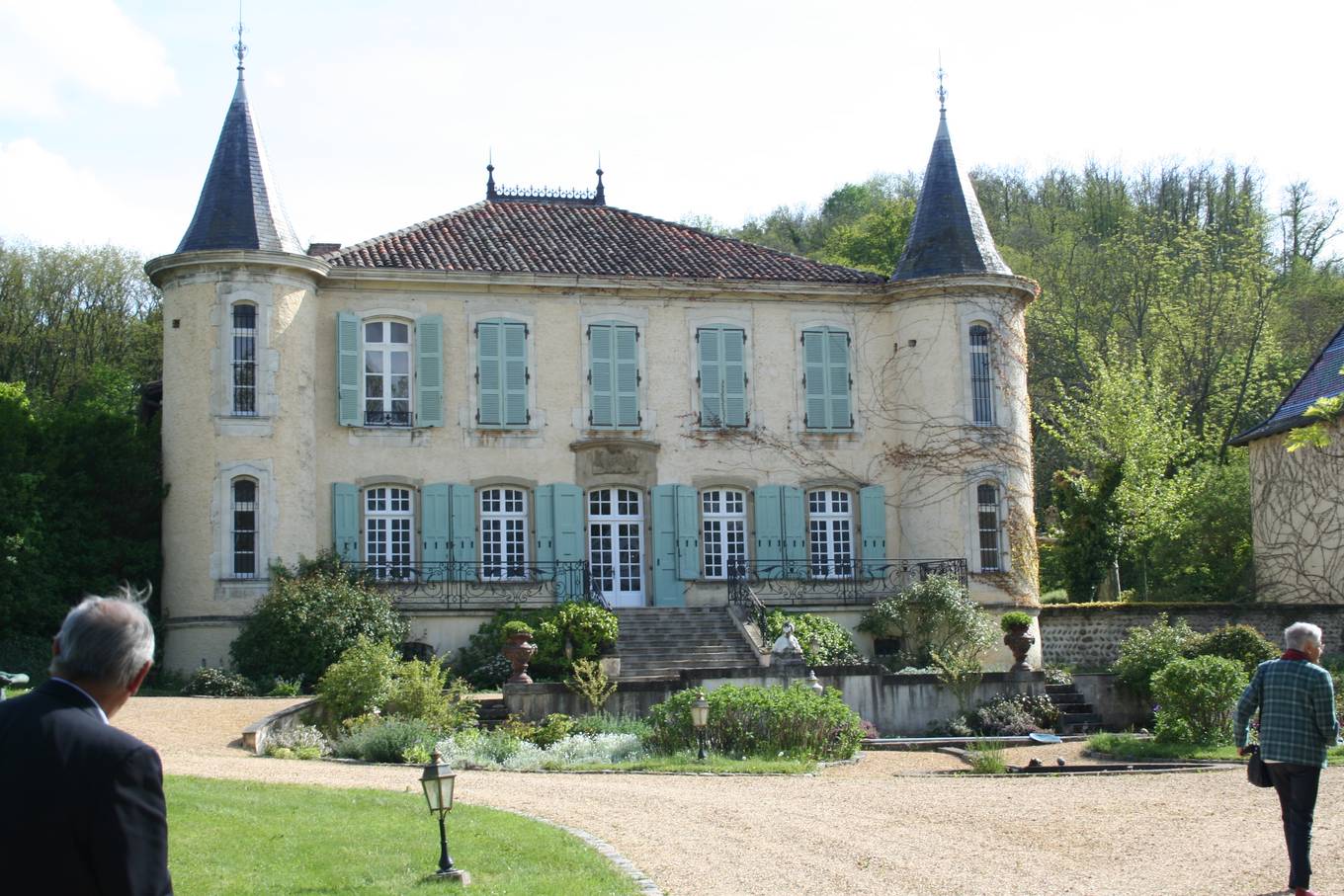 Le château du Double, façade claire à volets bleus encadrée de deux tours rondes à toit pointu, devant un parterre