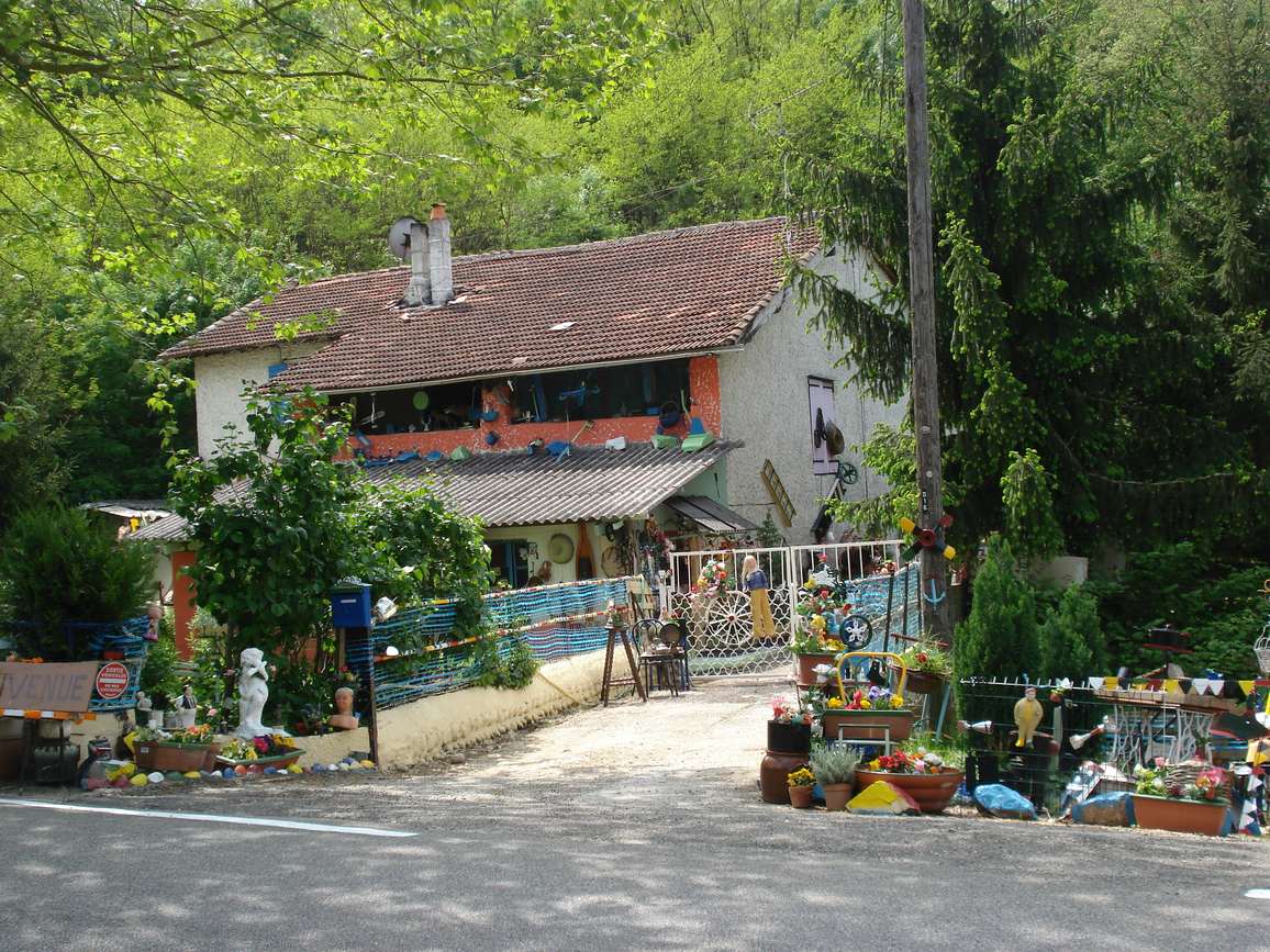 Une maison au bord d'une route, couverte d'objets de brocante peints de couleurs vives, statues et pots devant la façade