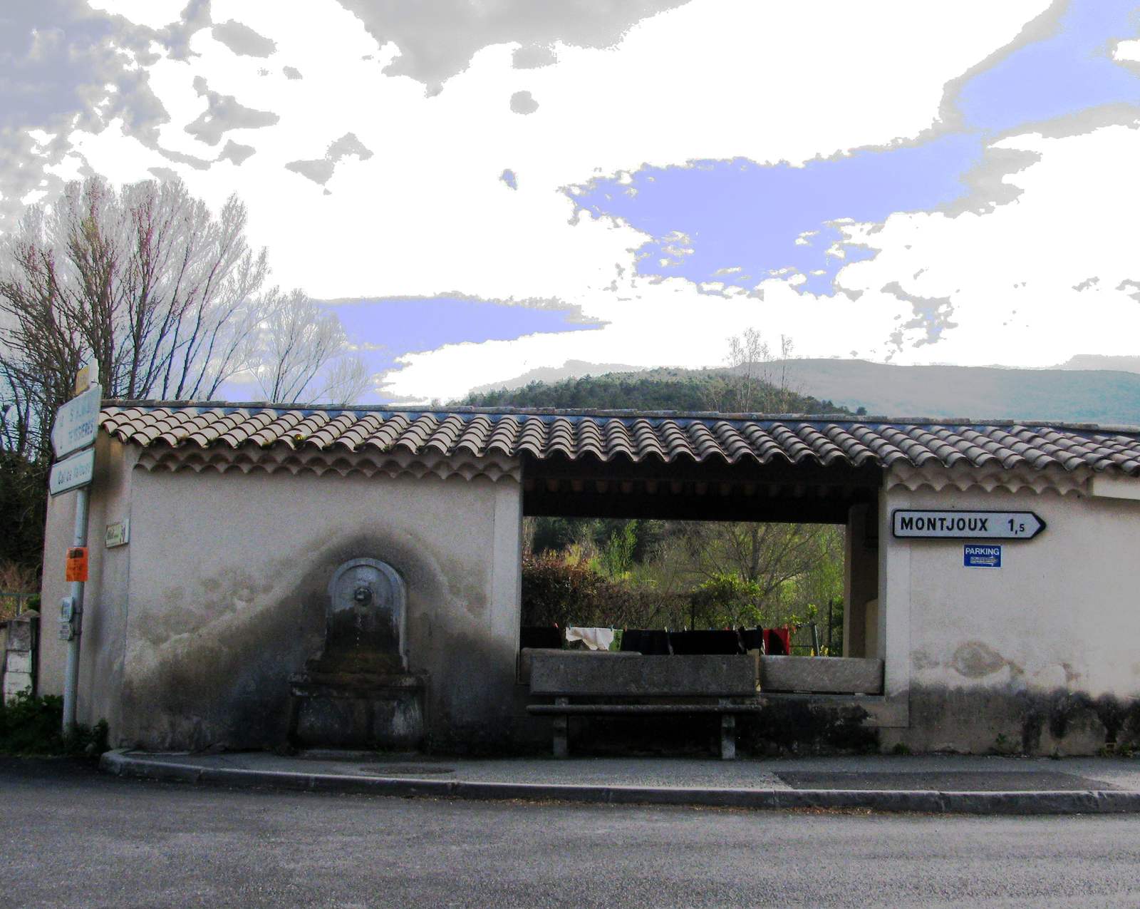 Le lavoir couvert de La Paillette à Montjoux, sa fontaine et ses bassins, avec un panneau routier indiquant Montjoux à 1,5 km