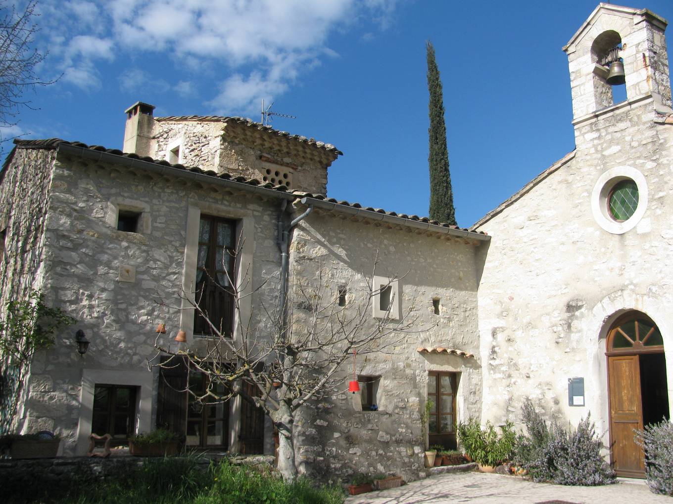 La place du vieux village de Montjoux, avec un pigeonnier percé de boulins à gauche et l'église Saint-Étienne à clocher-mur à droite