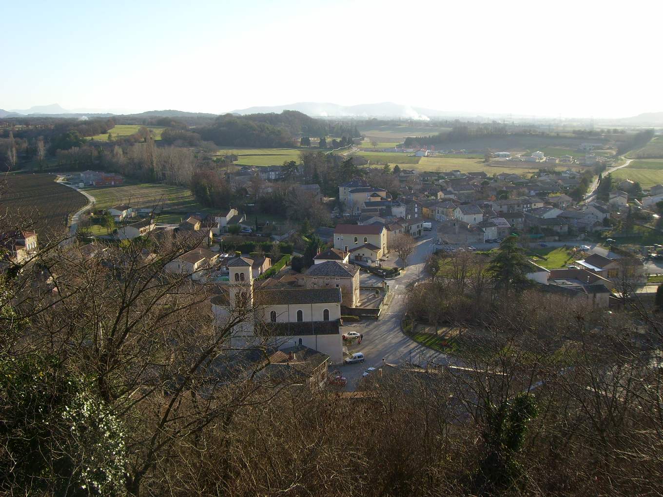 Vue plongeante sur Montvendre depuis le calvaire, l'église et son clocher au centre, les maisons du village et la plaine de Valence jusqu'aux montagnes