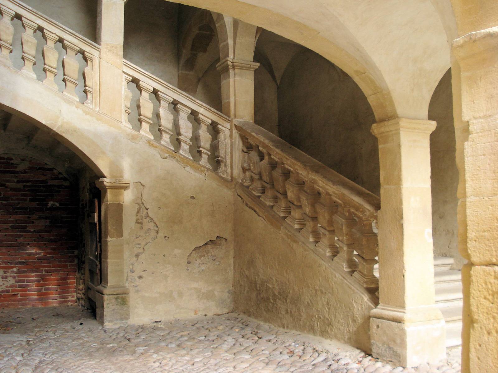 Escalier de pierre à volées droites et à balustres, sous des arcades, dans une cour de Moras-en-Valloire