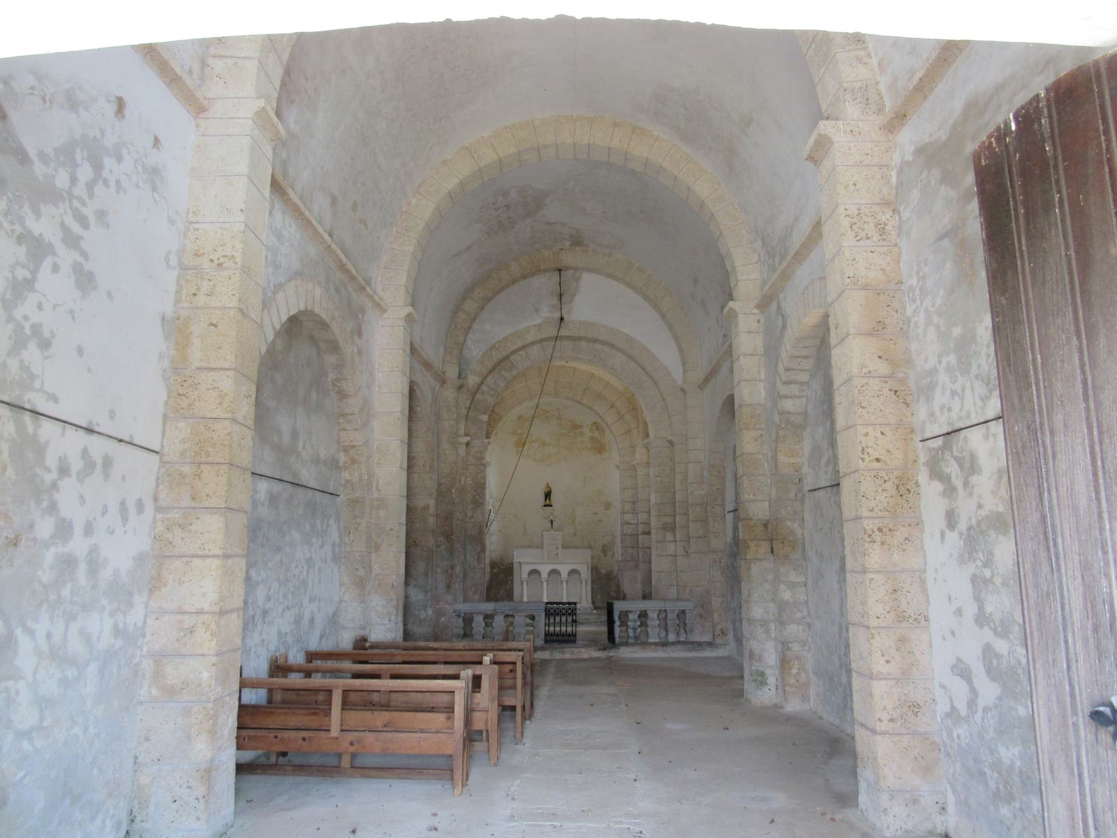 L'intérieur blanc de la chapelle Saint-Pierre, une nef voûtée sur arcs de pierre clairs, quelques bancs de bois et l'autel au fond de l'abside