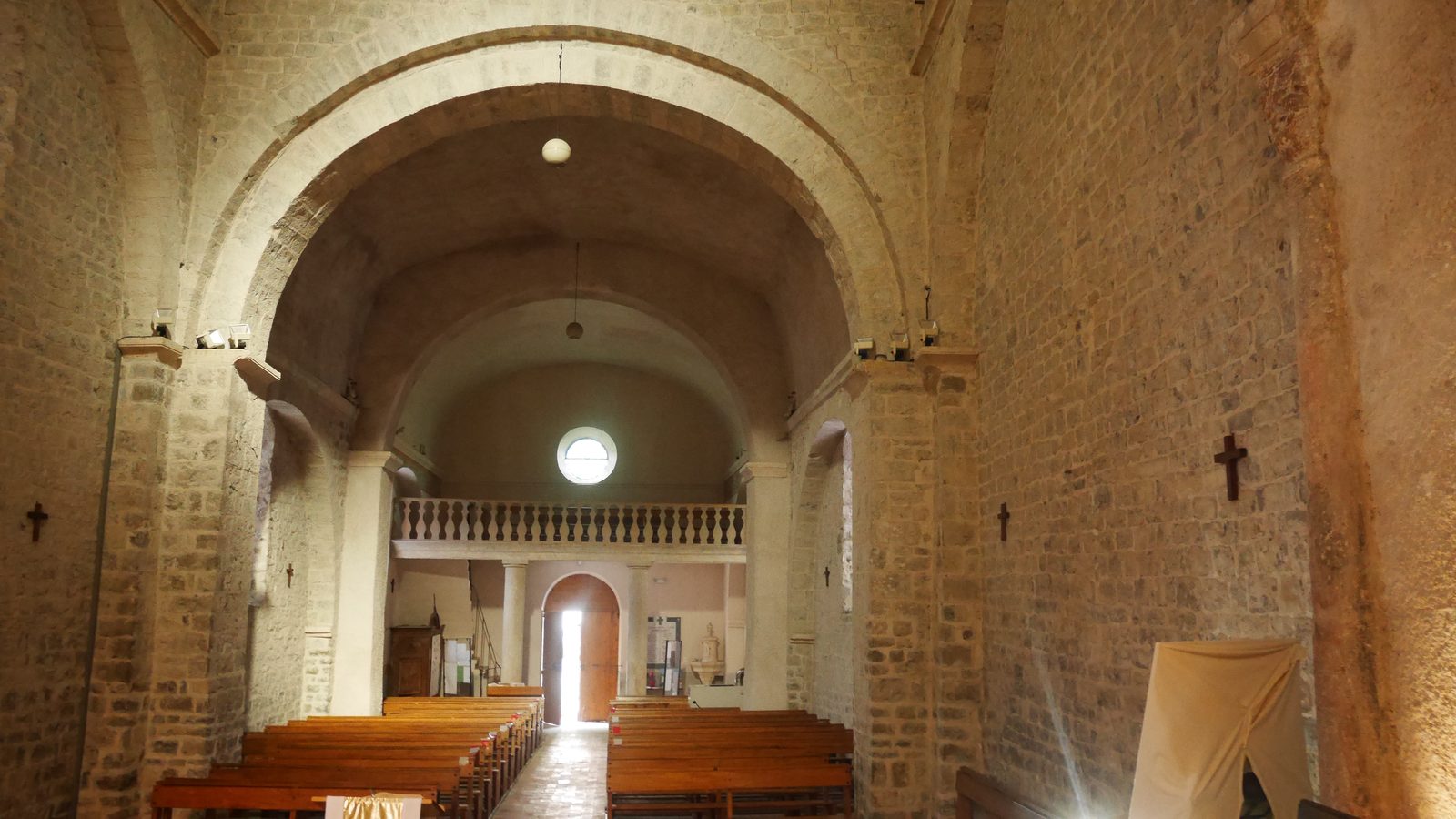 La nef de l'église Notre-Dame de La Clastre, murs de pierre claire et grand arc roman, avec les bancs et la tribune au fond