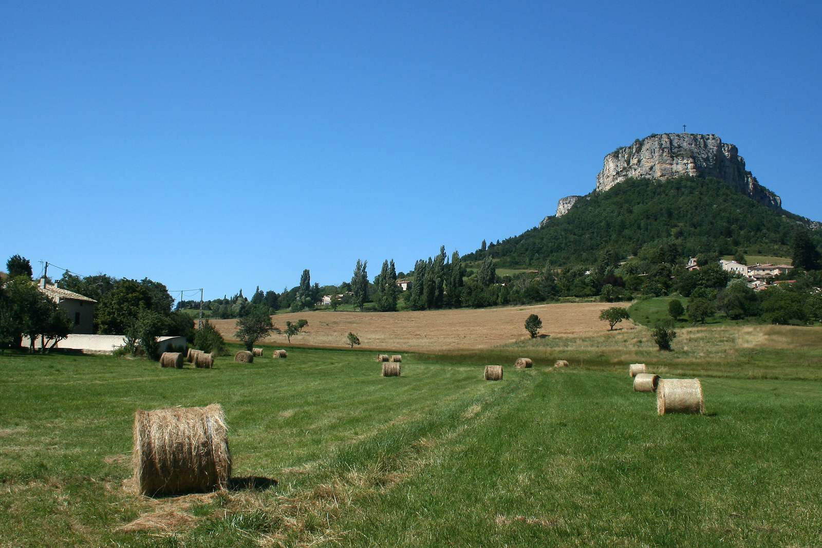 Le rocher du Vellan et sa croix au-dessus du village de Plan-de-Baix, prairies de fauche au premier plan