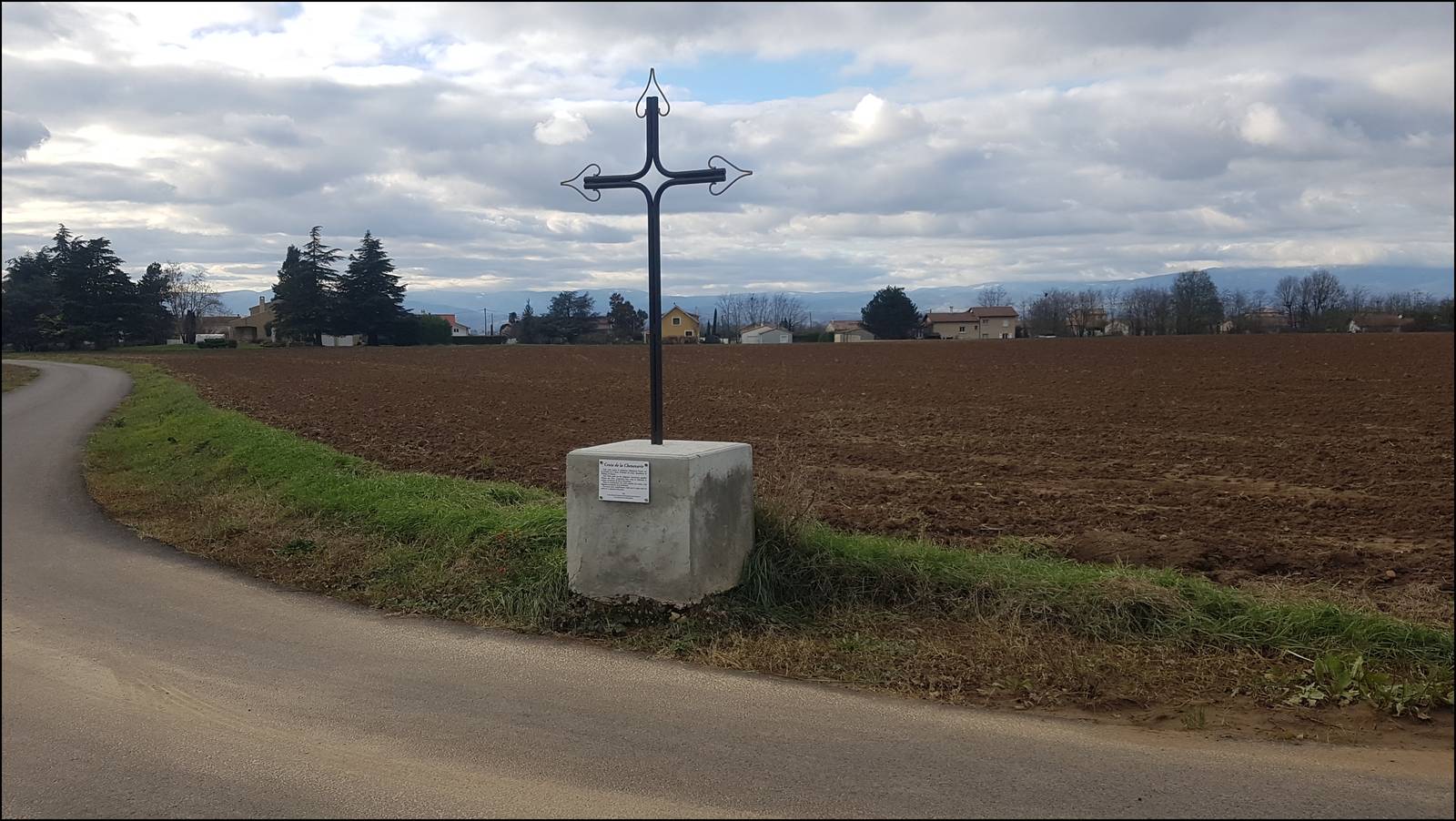 La croix de fer forgé de la Chenevarie au bord d'un chemin de la plaine de la Valloire, devant un champ labouré