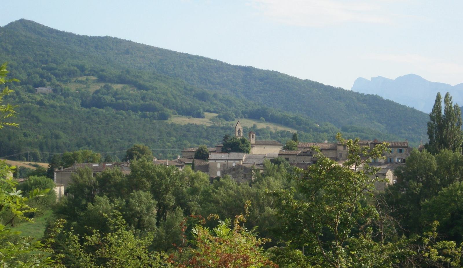 Le village de Sainte-Croix en Diois, son clocher-mur, les versants boisés et les falaises du Vercors au fond