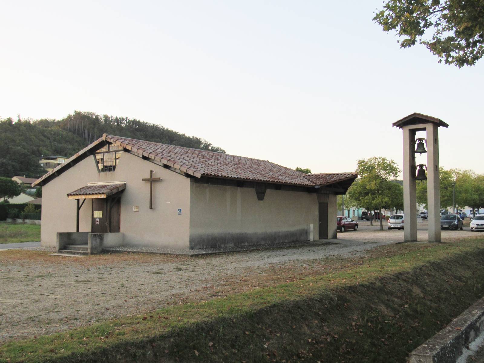 L'église Saint-Sébastien de Triors, bâtiment bas et simple à toit de tuiles avec une croix sur la façade, et à côté un clocher isolé en béton portant deux cloches